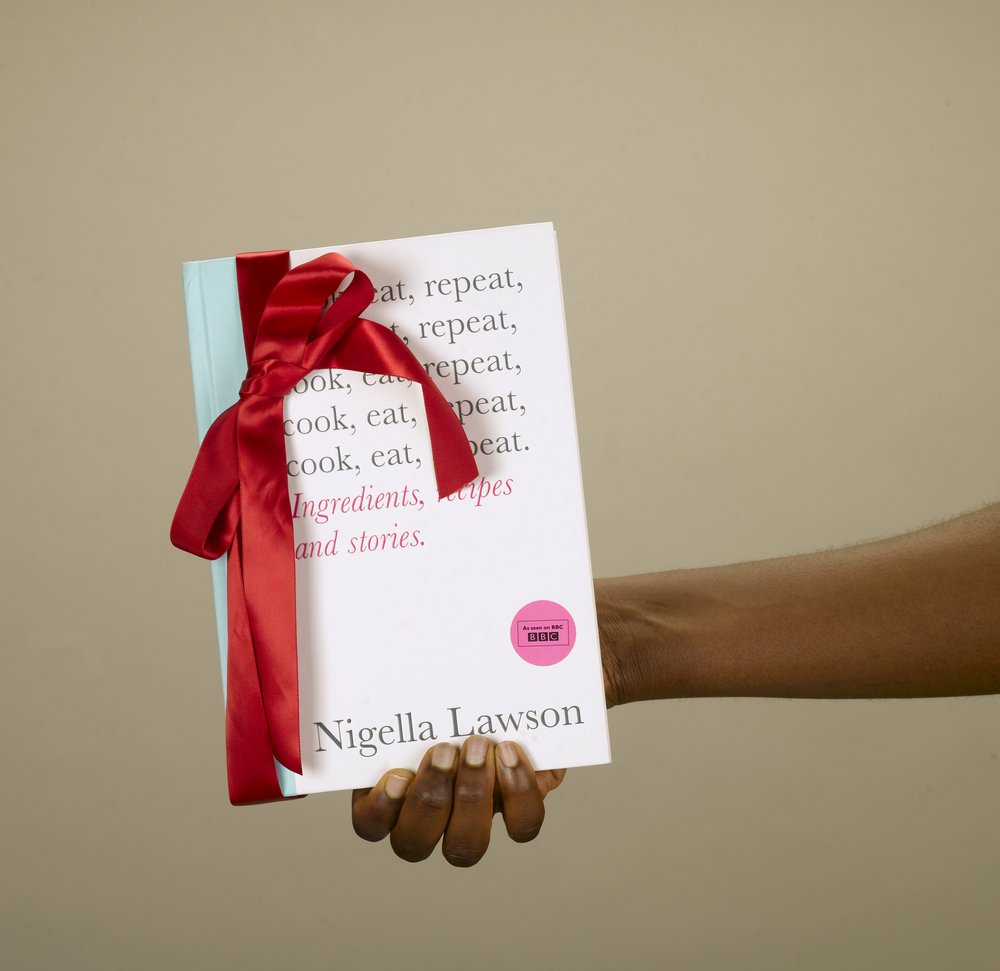 A hand holding a Nigella recipe book wrapped with a red bow