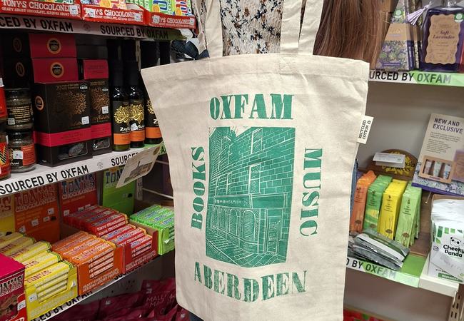 Oxfam volunteer modelling the tote bag inside the Back Wynd shop
