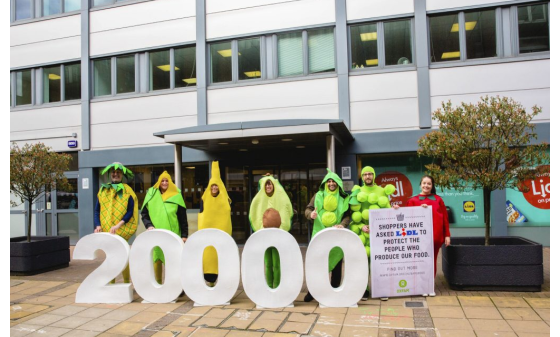 A group of campaigners dresses as fruit holding a bit number '20000' and a placard reading "Shoppers have asked Lidl to protect the people who produce our food".