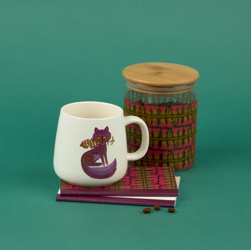 Belinda Lyon mug on top of some notebooks and a storage jar all featuring a Belinda Lyon-inspired design