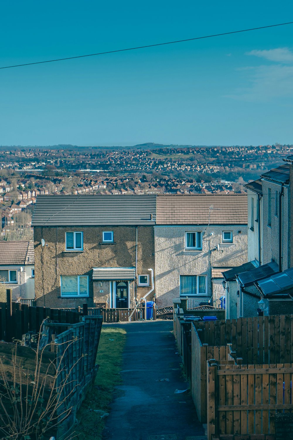 Image of a lane leading to council houses. Blue sky and view over the rest of the town below