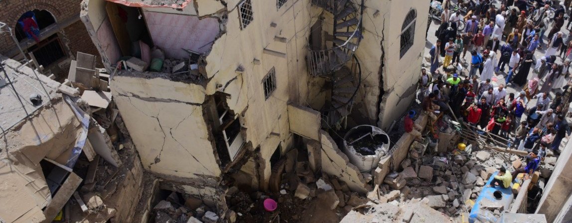 Civilian houses destroyed with groups of people stood around looking at the rubble.