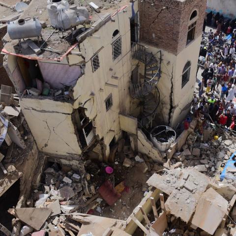 Civilian houses destroyed with groups of people stood around looking at the rubble.