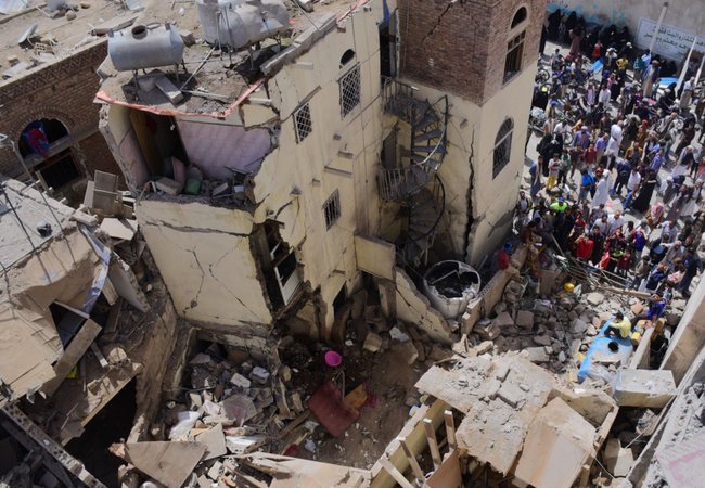 Civilian houses destroyed with groups of people stood around looking at the rubble.