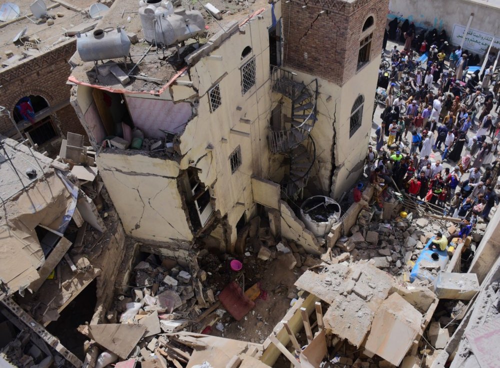 Civilian houses destroyed with groups of people stood around looking at the rubble.