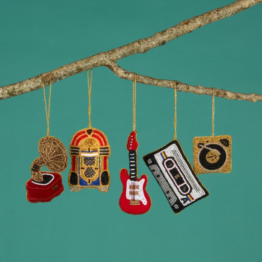 Intricately beaded Christmas decorations hanging from a branch. The designs include a gramophone, jukebox, electric guitar, cassette and vinyl record player.