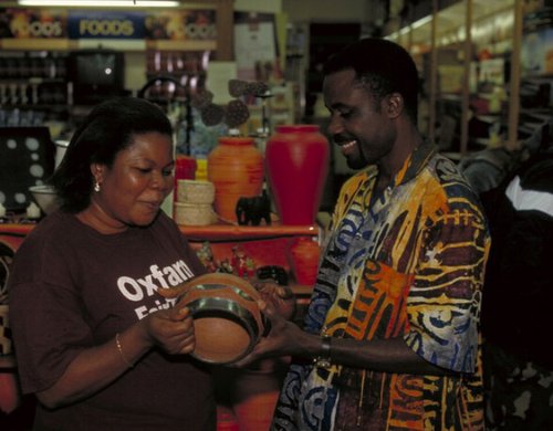 A smiling man hands a woman in an Oxfam t-shirt an African vase.
