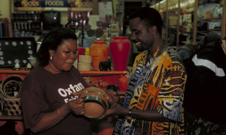 A smiling man hands a woman in an Oxfam t-shirt an African vase.