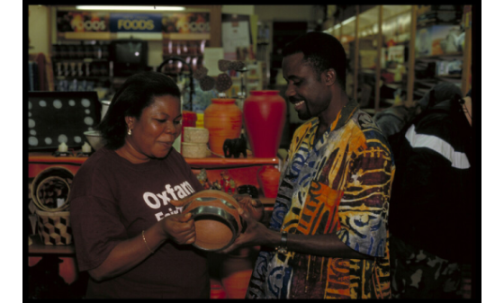 A smiling man hands a woman in an Oxfam t-shirt an African vase.