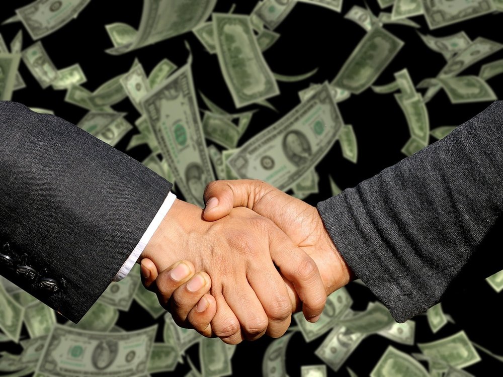 Two male hands in a handshake pose with a background of dollar bills floating down.