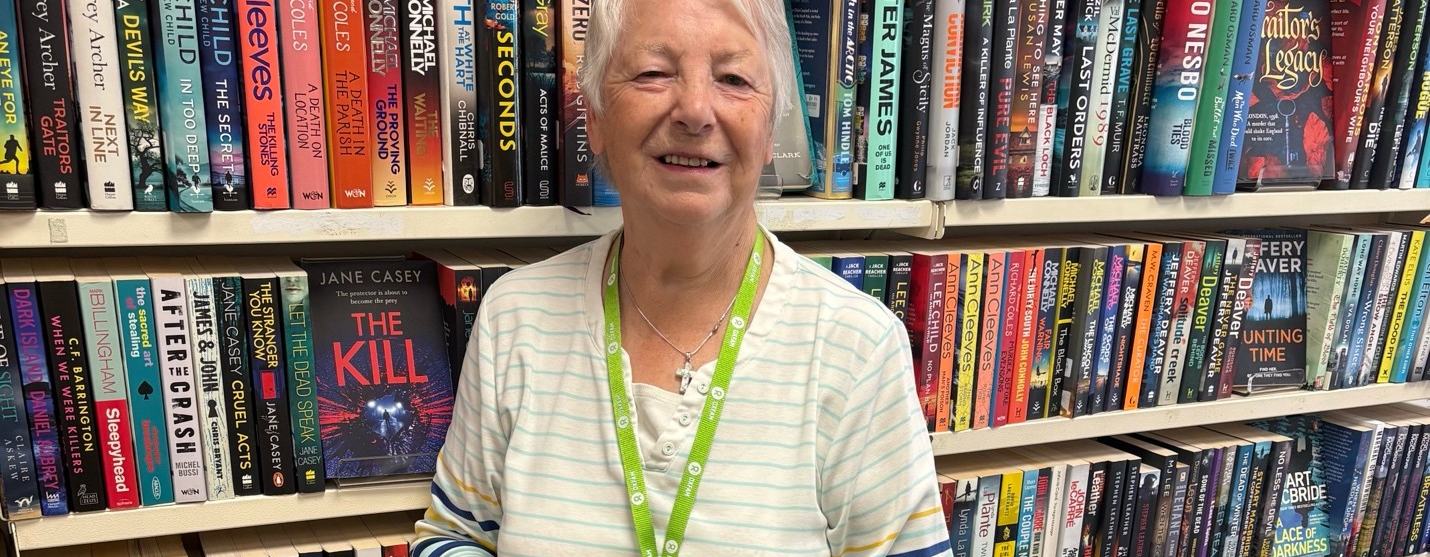 Image of Helen standing in front of a bookshelf holding a book titled 'In the dead of winter'