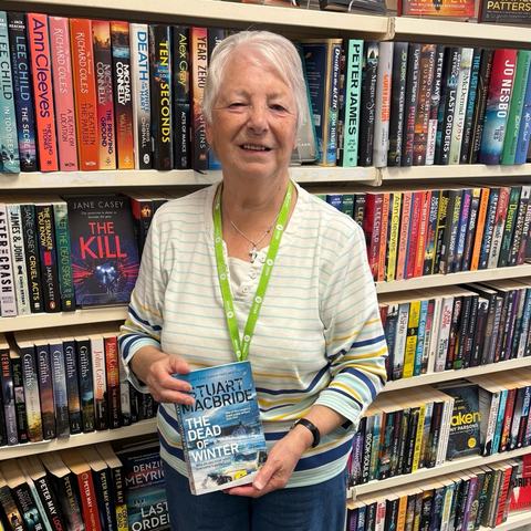 Image of Helen standing in front of a bookshelf holding a book titled 'In the dead of winter'