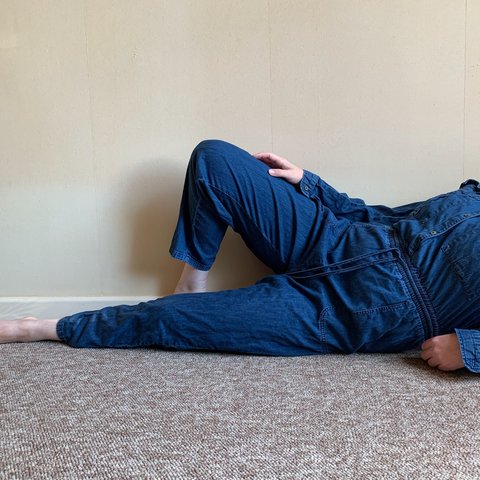 A person lying down with a knee bent wearing a denim boilersuit. Their face cannot be seen.