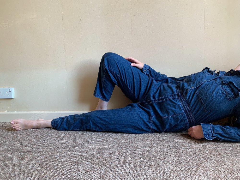 A person lying down with a knee bent wearing a denim boilersuit. Their face cannot be seen.