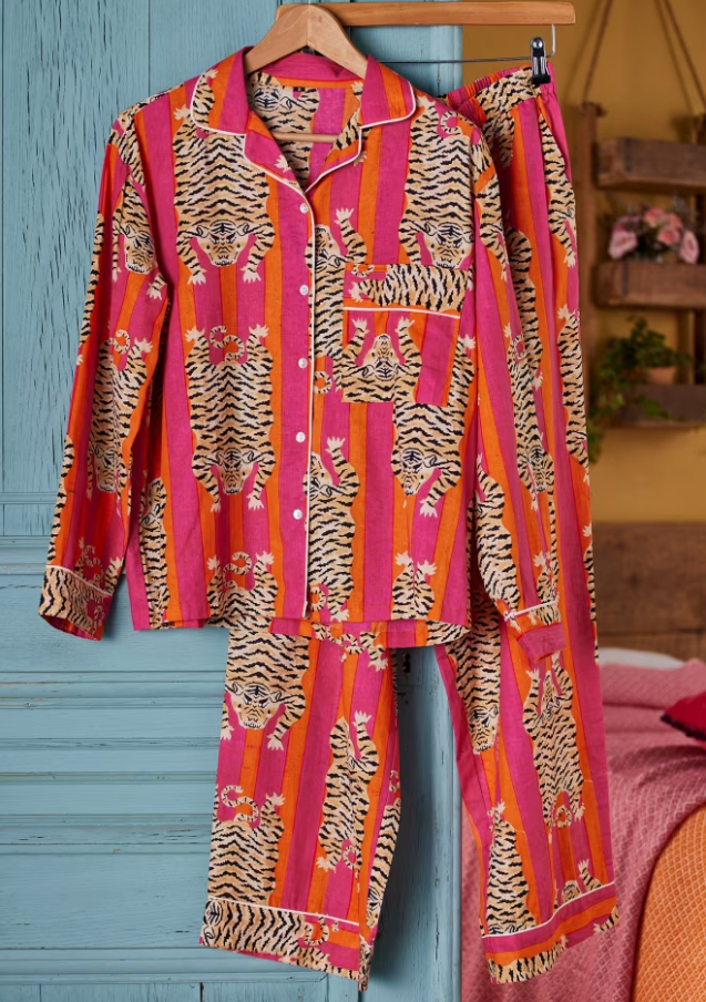 Bright pink pyjamas with a tiger print hanging on a wooden hanger.