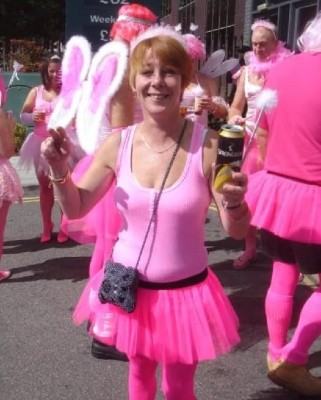 Lisa is outside a venue wearing a pink leotard and pink tutu skirt with other people in the background dressed in similar clothes.