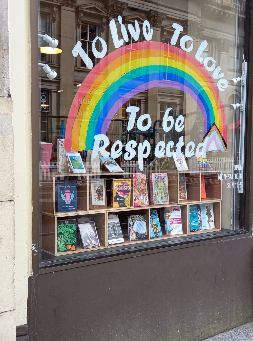 An Oxfam shop window with the words in rainbow colours 'live, love, be respected'