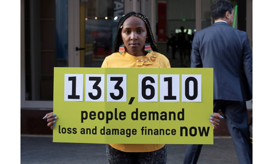 Climate activist Elizabeth Wathuti holds a sign reading '133,610 people demand loss and damage finance now'.
