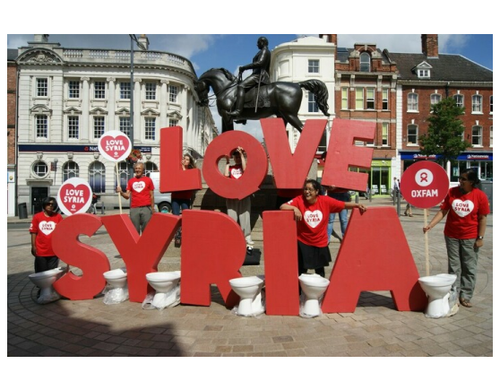 Campaigners in red Oxfam t-shirts stand next to huge letters spelling out the words 'Love Syria'