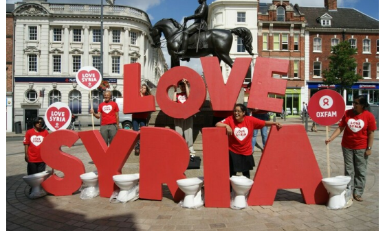 Campaigners in red Oxfam t-shirts stand next to huge letters spelling out the words 'Love Syria'