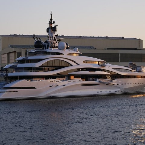 A super yacht moored with a very large building behind it and the sun setting