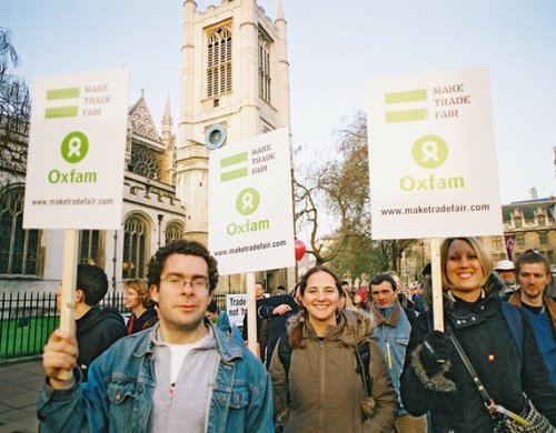 Smiling campaigners wave placards with the Oxfam logo reading 'Make trade fair'