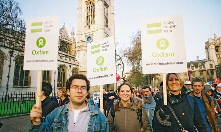Smiling campaigners wave placards with the Oxfam logo reading 'Make trade fair'