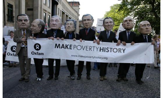 Campaigners wearing comically big masks of world leaders hold a banner reading 'Make Poverty History'