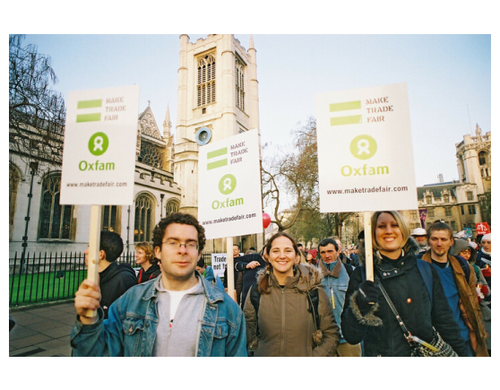 Smiling campaigners wave placards with the Oxfam logo reading 'Make trade fair'
