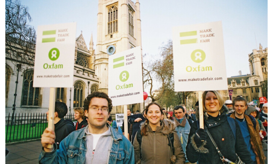 Smiling campaigners wave placards with the Oxfam logo reading 'Make trade fair'
