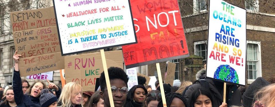 Young people hold up placards with information about how women and girls are being disproportionately impacted by climate change.