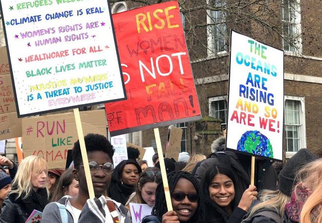 Young people hold up placards with information about how women and girls are being disproportionately impacted by climate change.