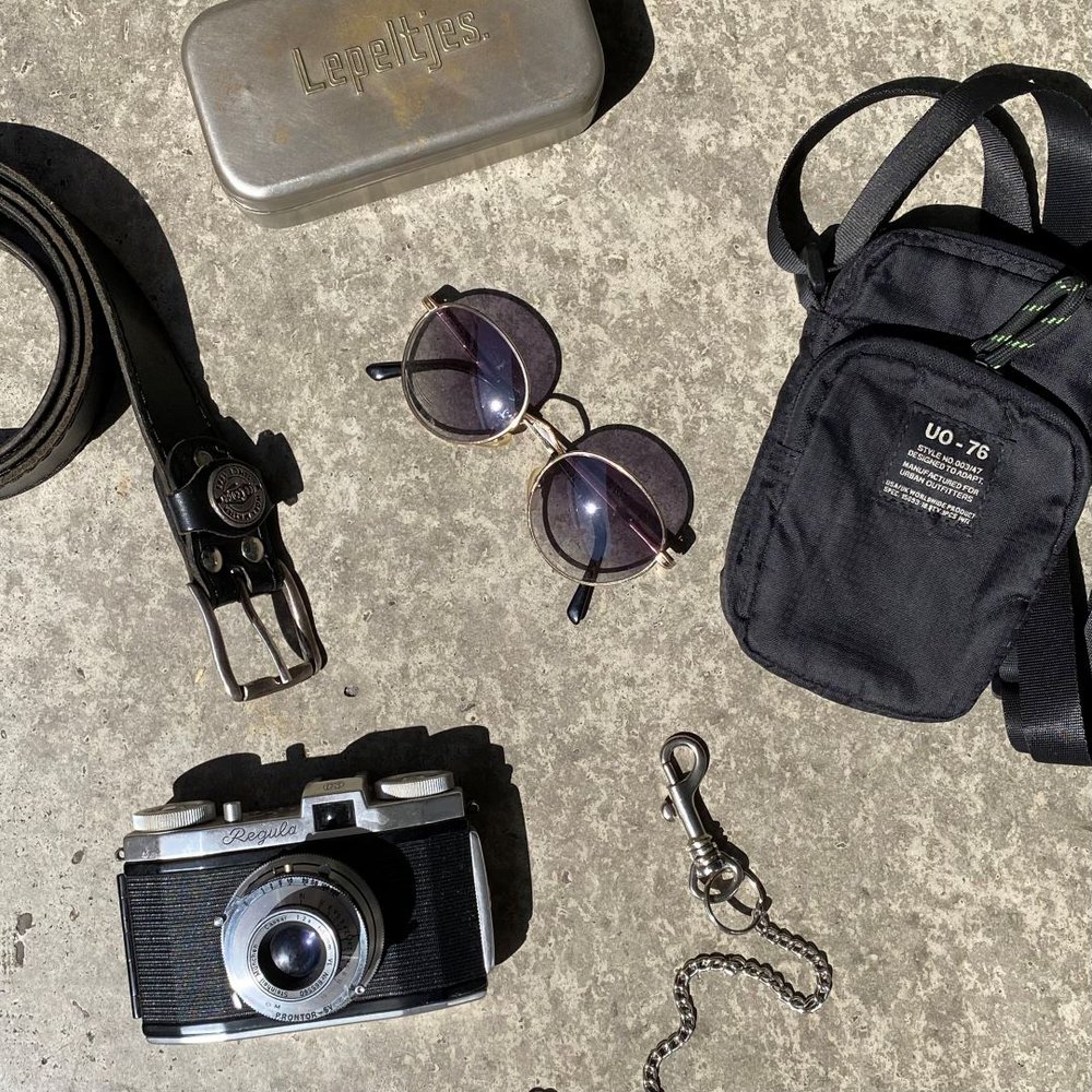 flaylay of men's accessories including a bag, sunglasses, belt chain and vintage camera