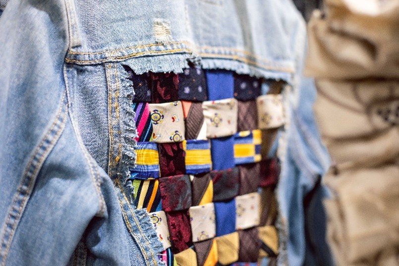 A close-up shot of a denim jacket showing an upcycled woven patchwork design made from old ties.