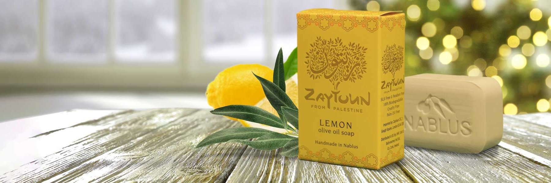 A bar of Zaytoun lemon olive oil soap sits on table with Christmas tree in the background