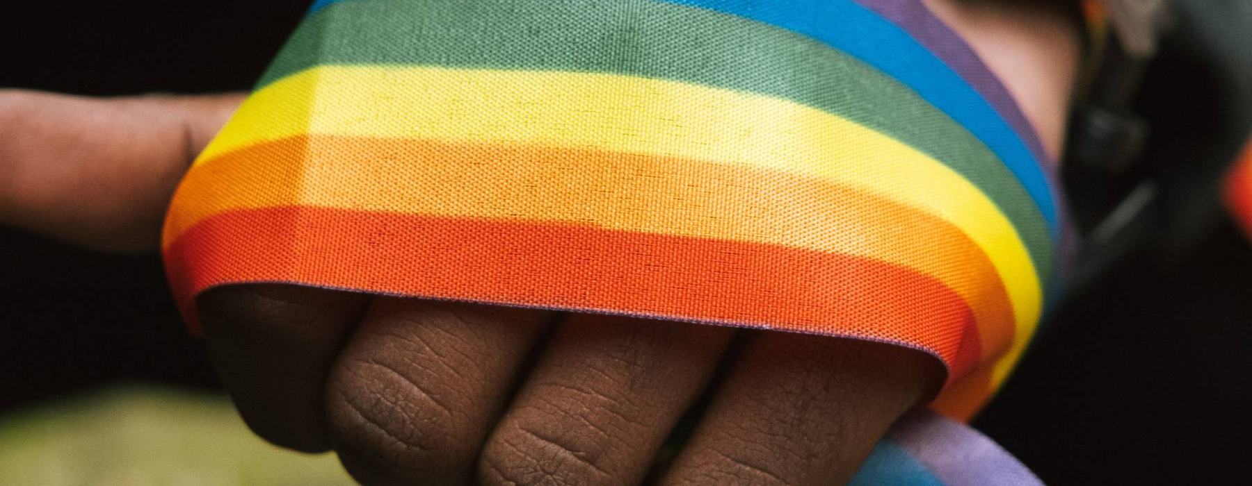 A thick band of rainbow coloured ribbon wrapped around the fist of a person of colour.