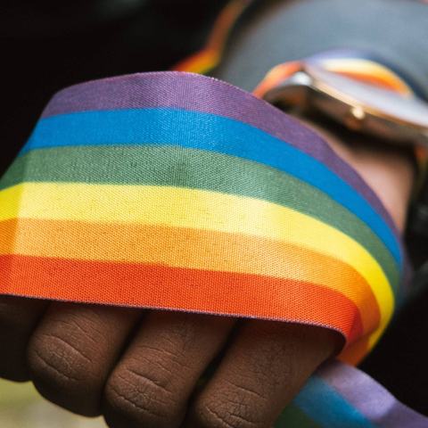 A thick band of rainbow coloured ribbon wrapped around the fist of a person of colour.