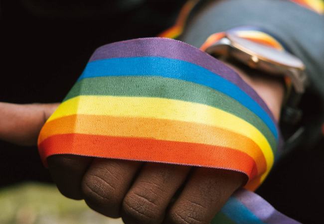 A thick band of rainbow coloured ribbon wrapped around the fist of a person of colour.