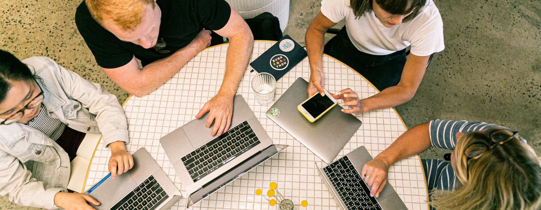 Four people sat around a table using laptop computers and smartphones