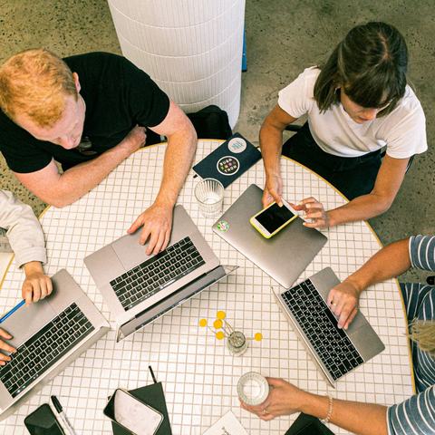 Four people sat around a table using laptop computers and smartphones