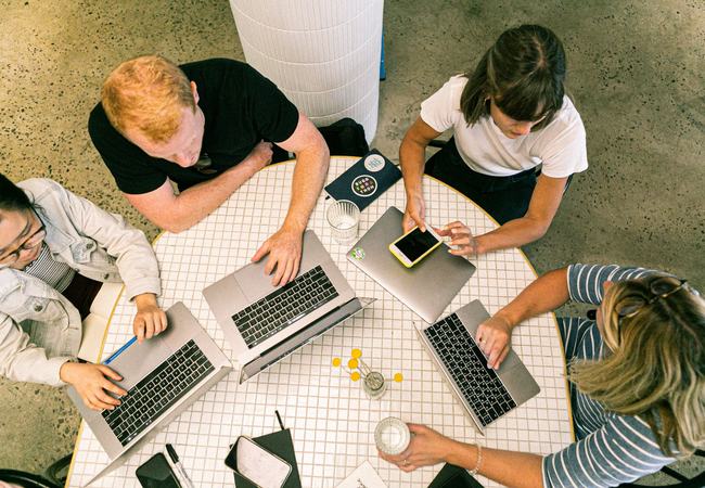 Four people sat around a table using laptop computers and smartphones