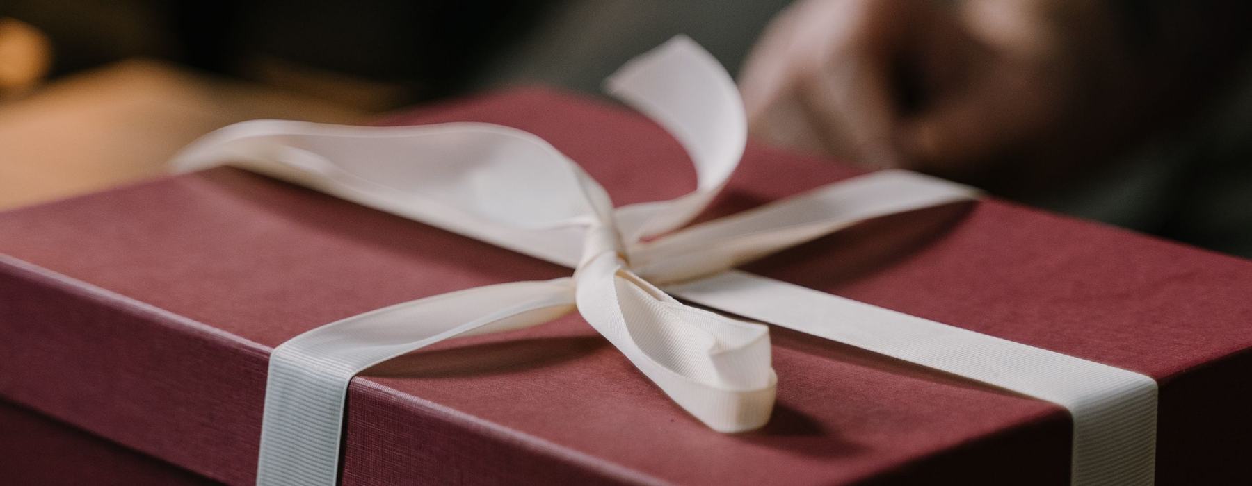 A burgundy present box wrapped with white ribbon sitting on a table