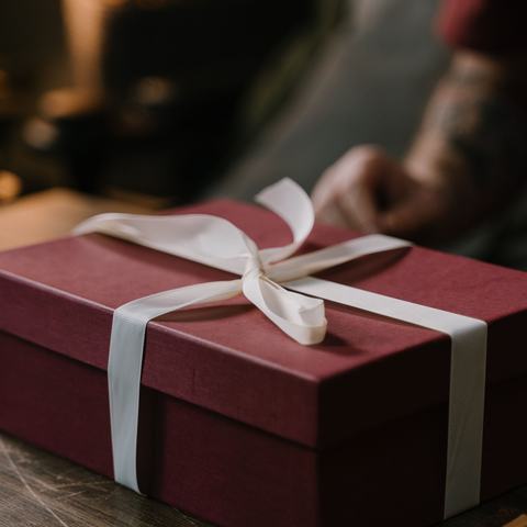 A burgundy present box wrapped with white ribbon sitting on a table