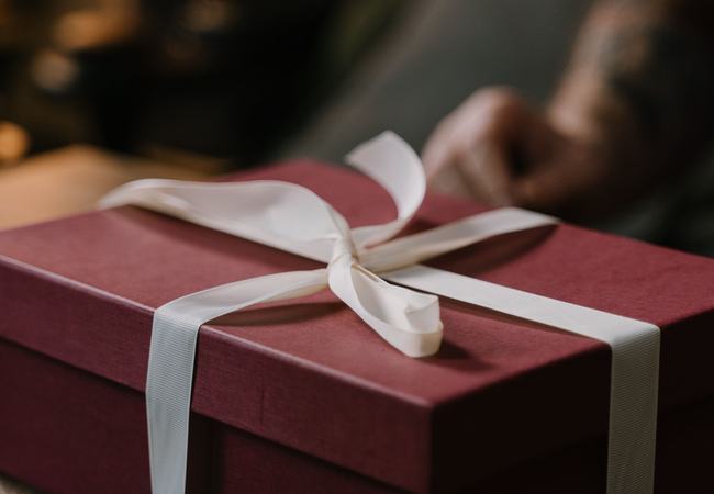 A burgundy present box wrapped with white ribbon sitting on a table