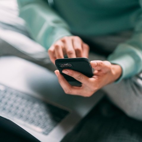 A person typing into a mobile device with an open laptop next to them.