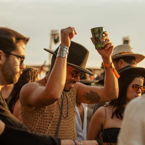 People in the middle of a music festival crowd dancing. The person is wearing a hat and a crochet top.