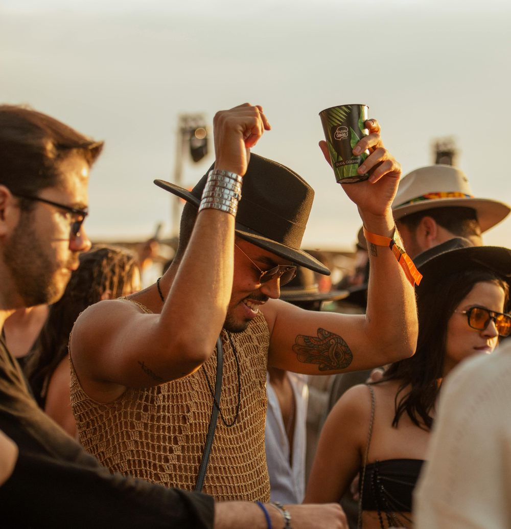 People in the middle of a music festival crowd dancing. The person is wearing a hat and a crochet top.
