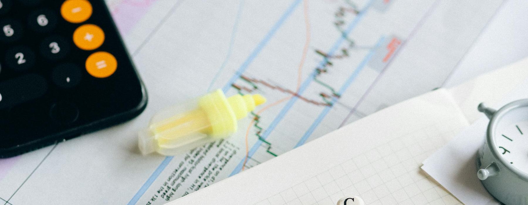 A desk with a sheet of paper showing a line graph with lots of peaks and troughs, a magnifying glass and coloured highlighters. There is also a pad with scrabble letters spelling C-H-A-N-G-E and a single letter C just above the G.