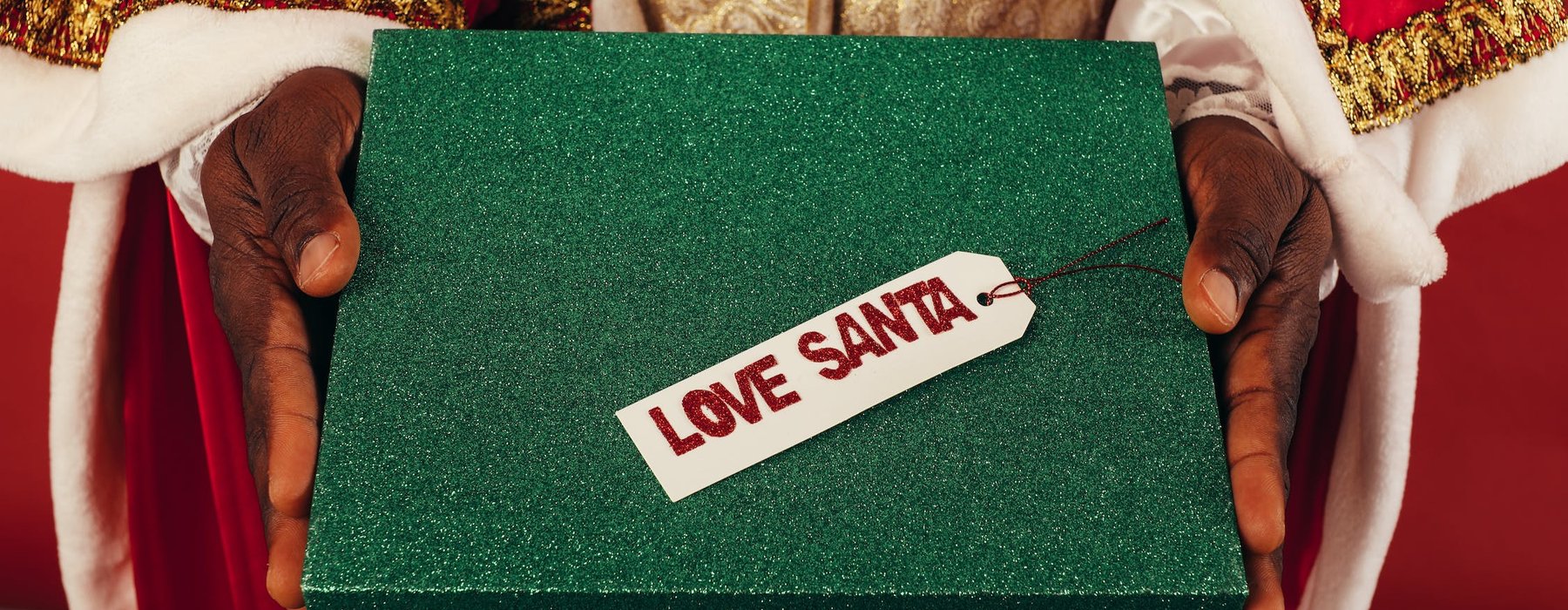 Santas hands passing a glittery green box that says Love Santa