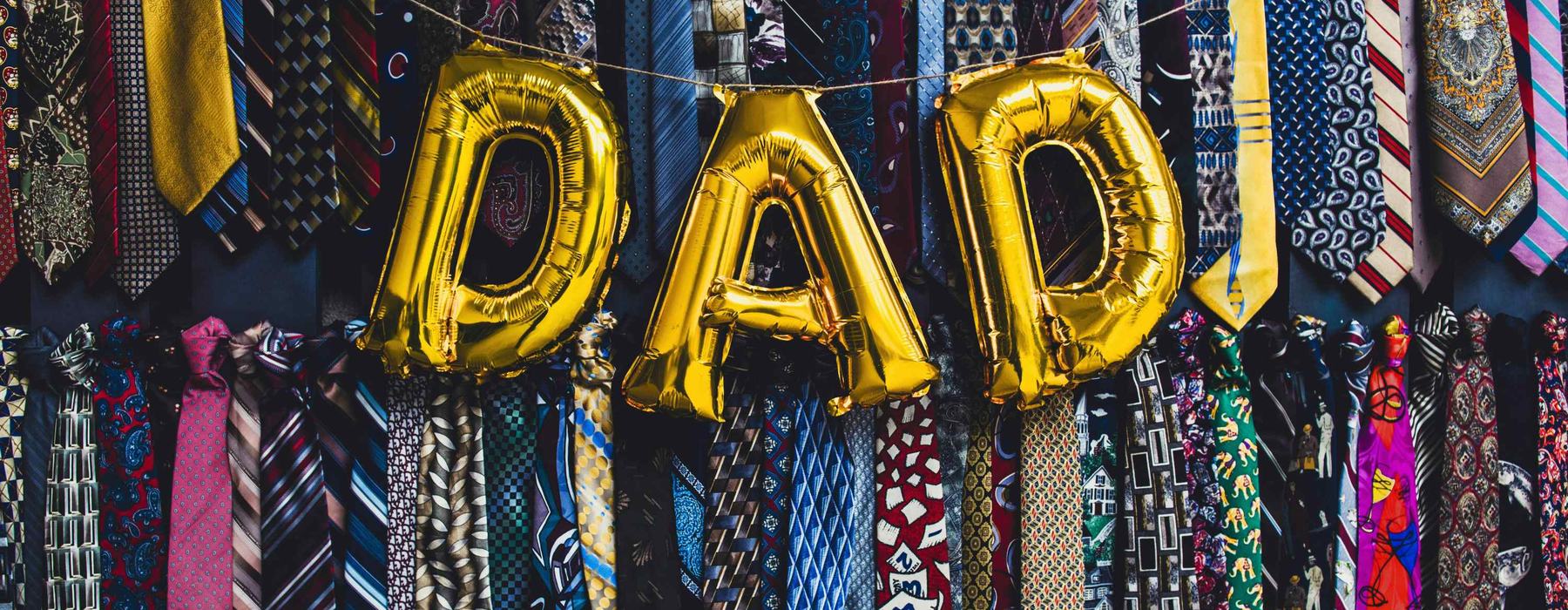 Gold balloons spelling out DAD, on a background of funky pattern ties all hung up. Two rows of around 40 ties.
